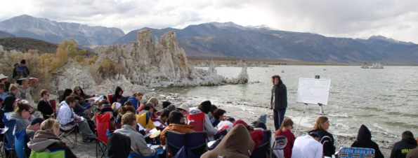 Students sitting next to lake listening to instructor